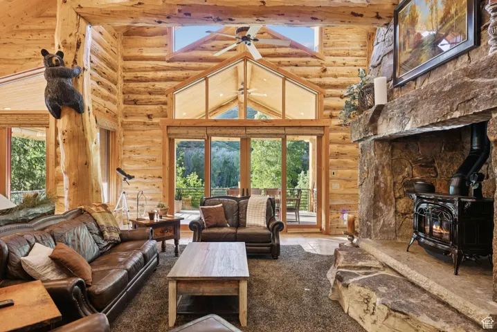 Living room with split-log walls, high vaulted ceiling, a wood stove, and tongue-in-groove ceiling