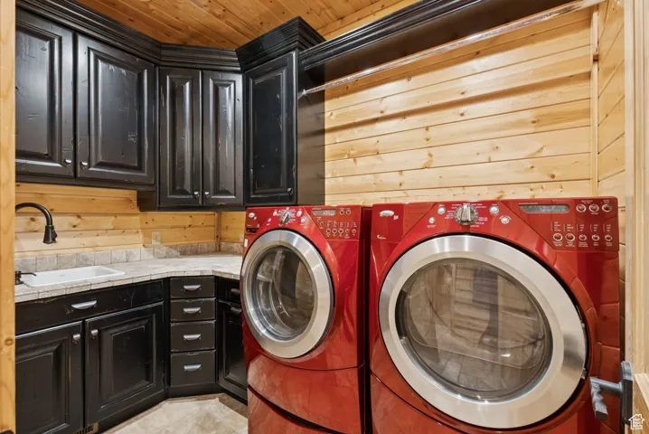 Laundry room featuring cabinet space, washing machine and dryer, wooden ceiling, and wooden walls