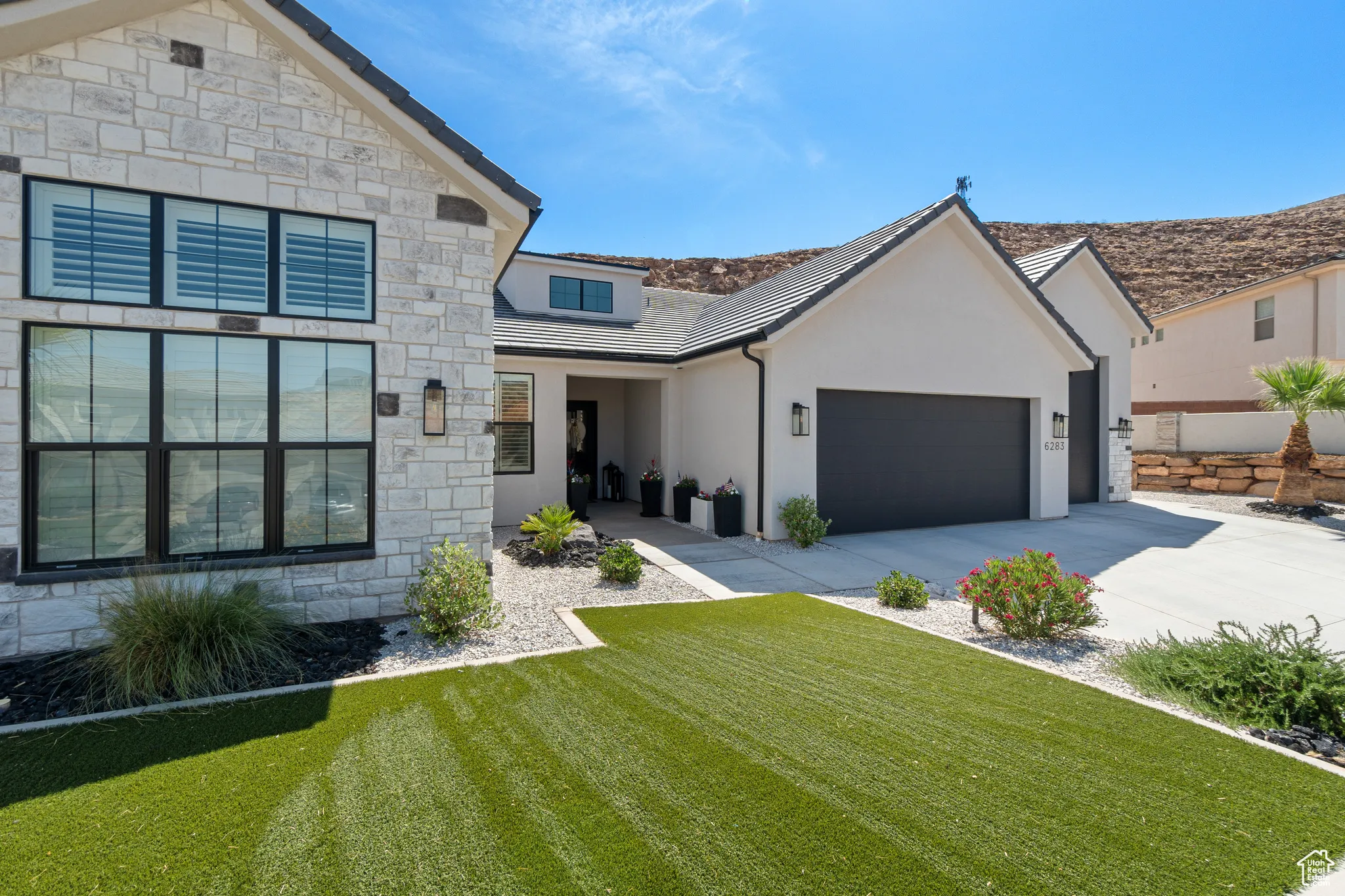 View of front facade featuring driveway, a front lawn, stucco siding, a garage, and stone siding