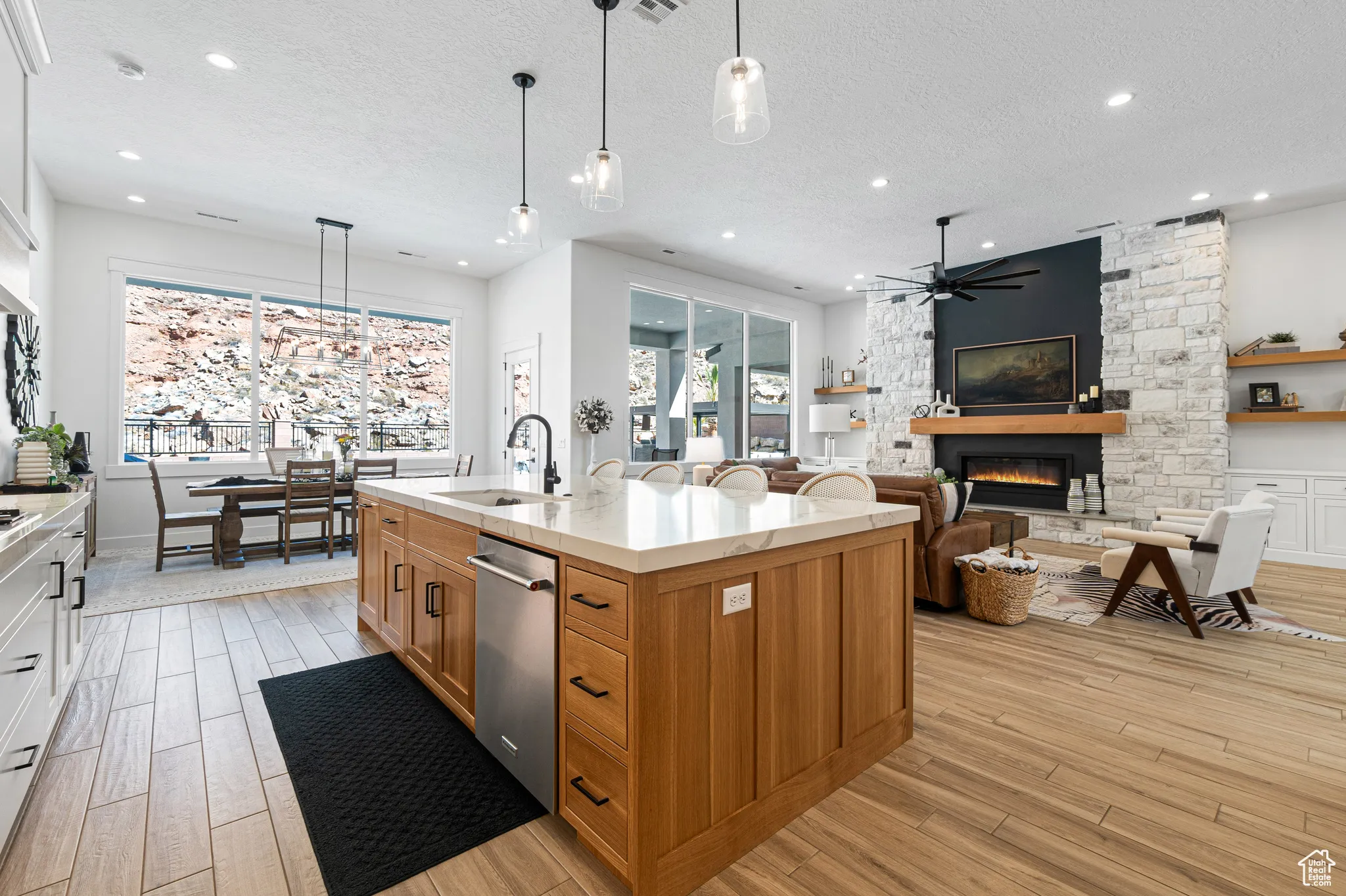 Kitchen with a stone fireplace, ceiling fan, stainless steel dishwasher, light wood-style floors, and a textured ceiling