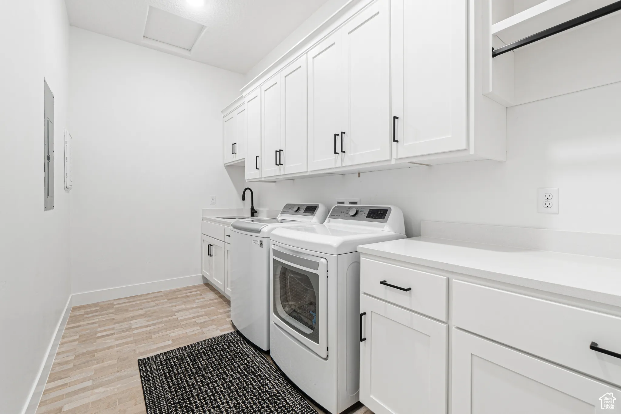 Washroom featuring washer and clothes dryer, cabinet space, light wood-type flooring, and electric panel