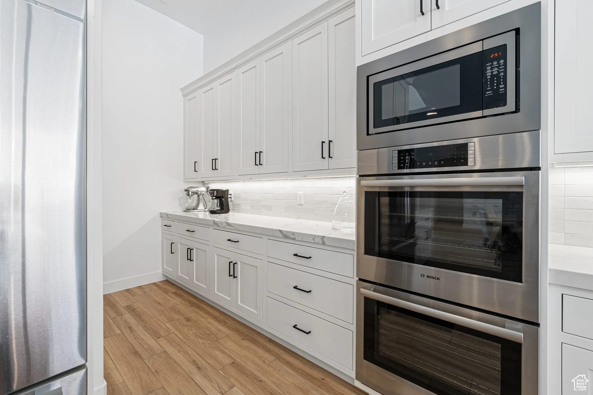 Kitchen with appliances with stainless steel finishes, backsplash, light wood finished floors, and white cabinetry