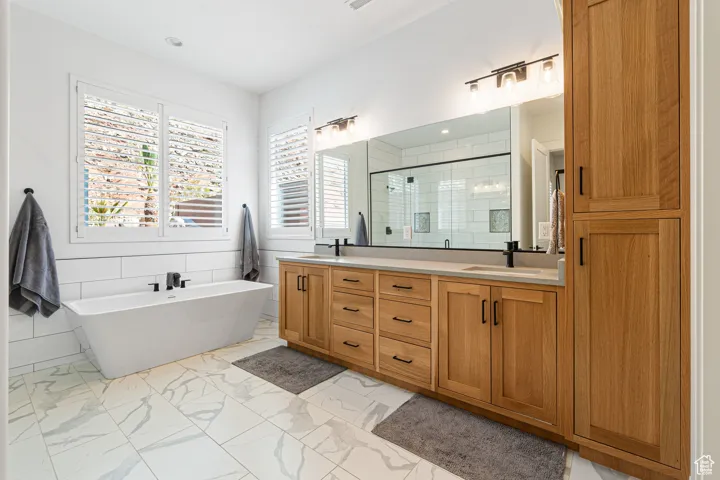 Full bath with a shower stall, double vanity, a soaking tub, marble finish flooring, and recessed lighting