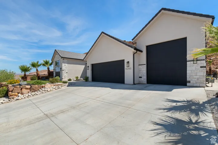 View of front of property with an attached garage, stone siding, stucco siding, and concrete driveway