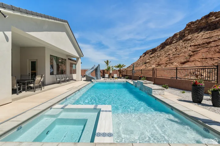 View of pool with a water slide, a fenced backyard, a patio area, a pool with connected hot tub, and a mountain view