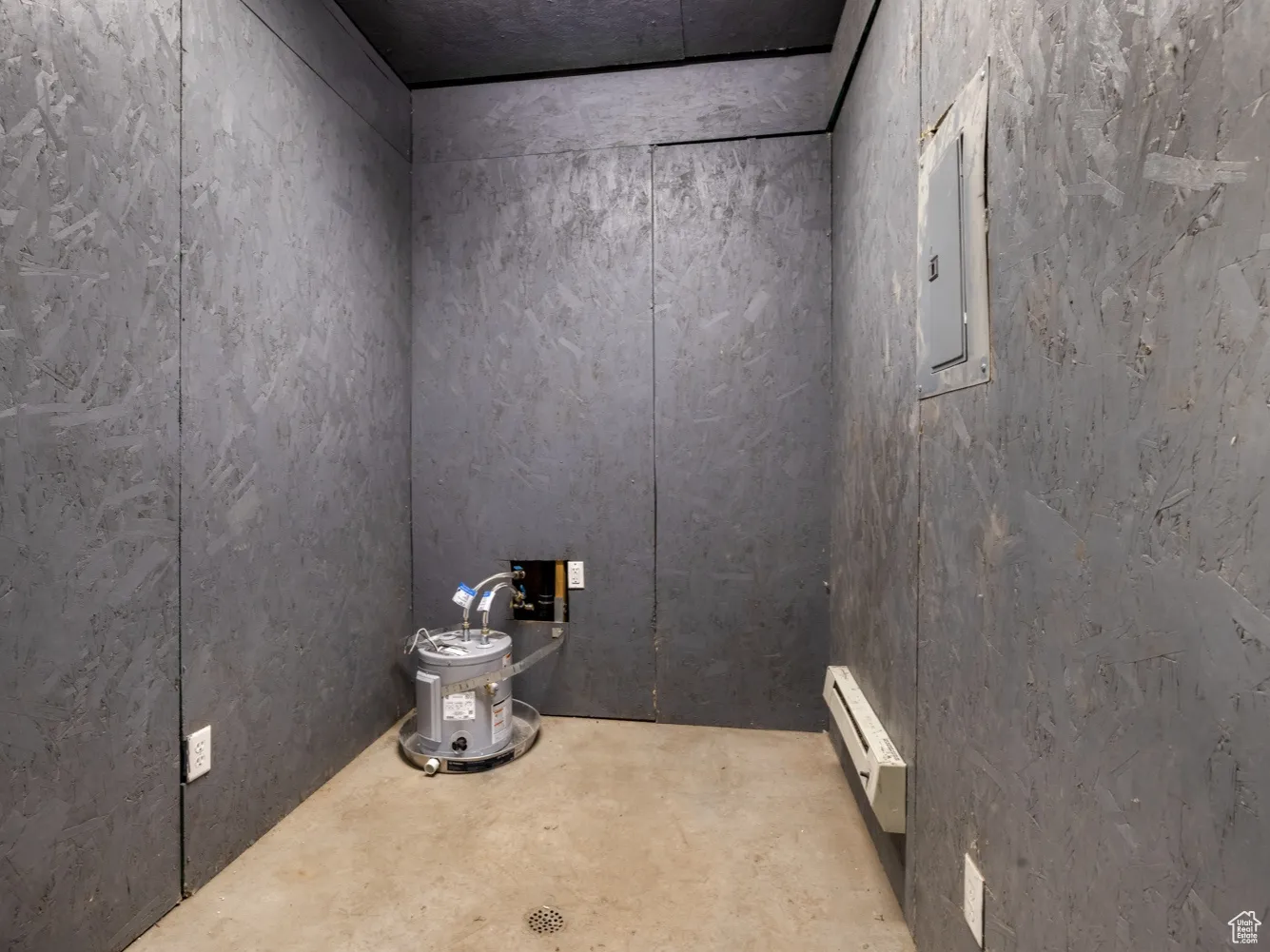Detailed view of baseboard heating, electric panel, and unfinished concrete flooring