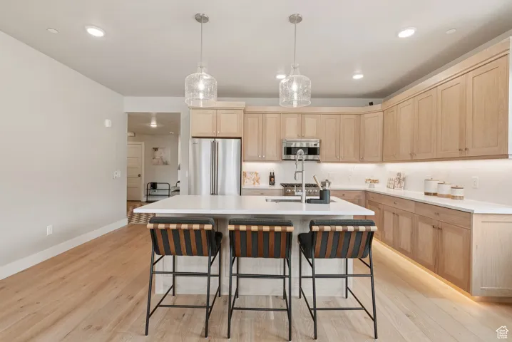 Kitchen featuring light brown cabinets, freestanding refrigerator, light wood finished floors, light countertops, and a breakfast bar