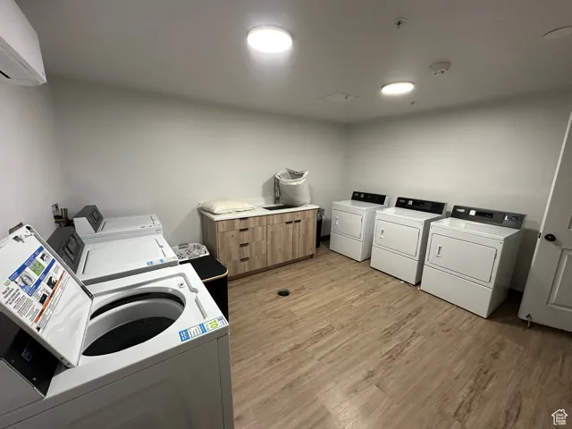 Shared laundry room with washer and dryer, light wood finished floors, and an AC wall unit