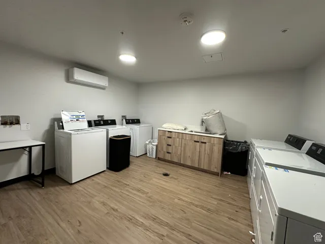 Community laundry with separate washer and dryer, an AC wall unit, and light wood-type flooring