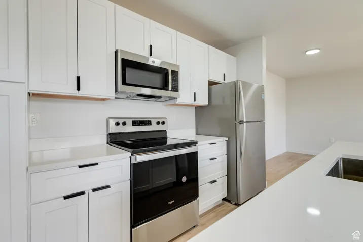 Kitchen featuring appliances with stainless steel finishes, light countertops, light wood-style flooring, white cabinetry, and recessed lighting