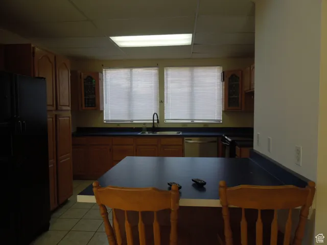 Kitchen with freestanding refrigerator, stainless steel dishwasher, a kitchen bar, a peninsula, and dark countertops