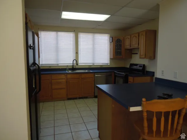 Kitchen with black electric range oven, dishwasher, dark countertops, a paneled ceiling, and a breakfast bar area