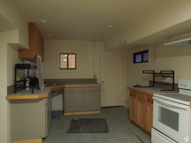 Kitchen with electric range, unfinished concrete floors, light countertops, brown cabinets, and recessed lighting