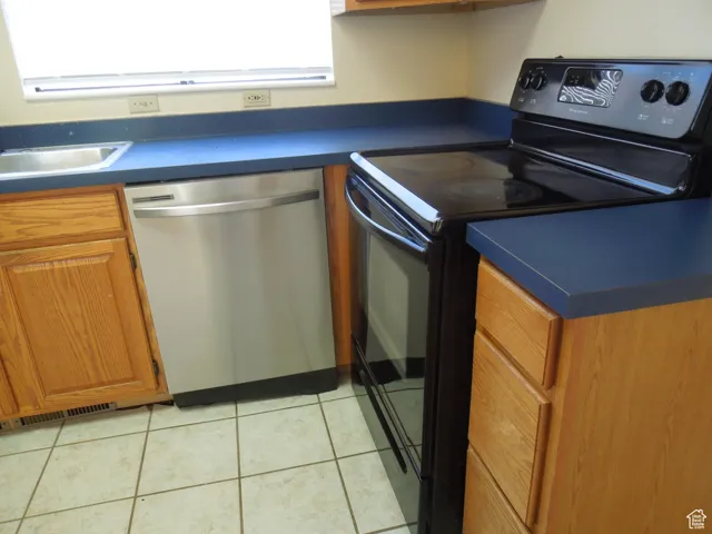 Kitchen with dishwasher, black range with electric cooktop, dark countertops, brown cabinets, and light tile patterned floors