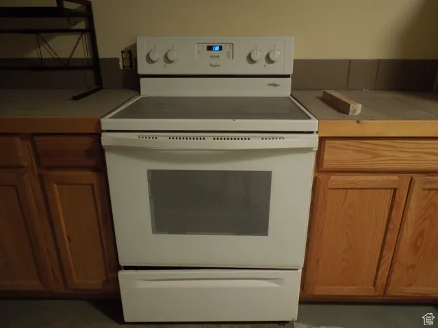Kitchen with white range with electric stovetop, brown cabinets, and tile counters