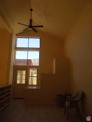 Tiled empty room with a ceiling fan, plenty of natural light, and high vaulted ceiling