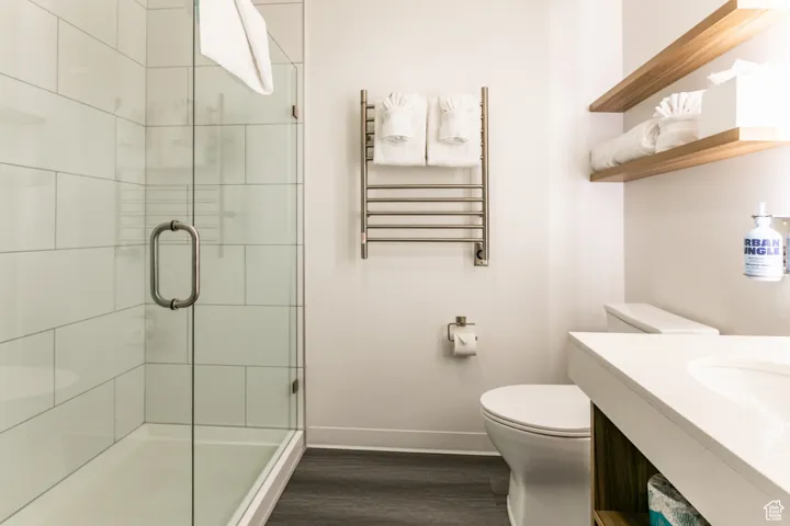 Bathroom with radiator, wood finished floors, a shower stall, vanity, and a towel warmer