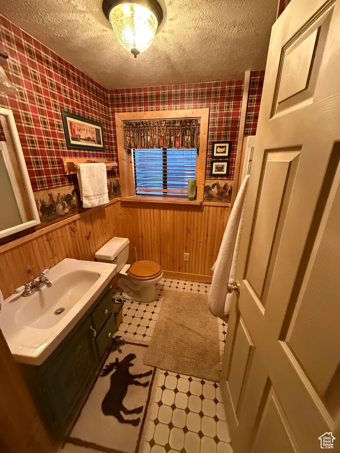 Half bathroom featuring tile patterned floors, wainscoting, wallpapered walls, a textured ceiling, and vanity
