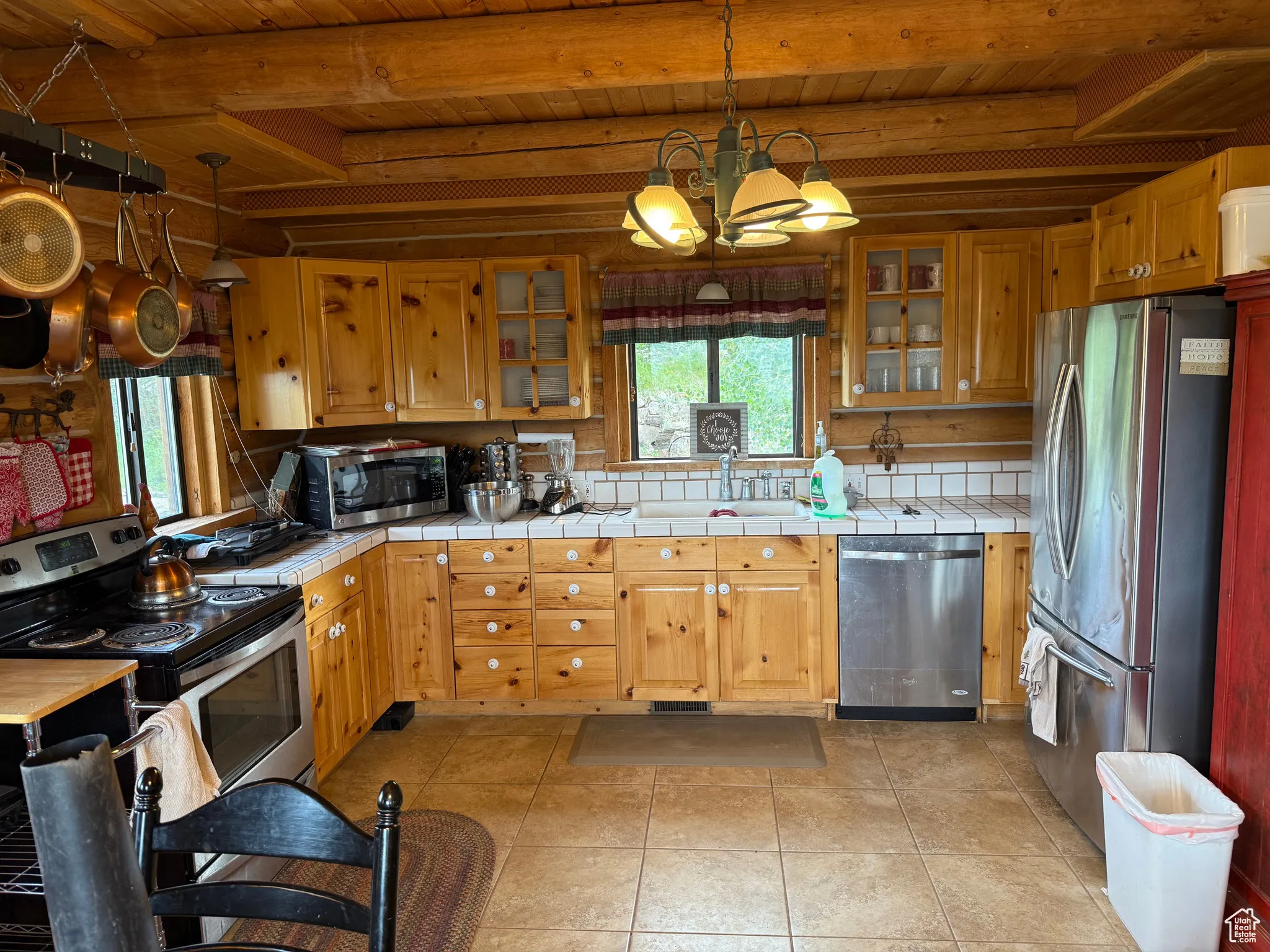 Kitchen featuring appliances with stainless steel finishes, tile countertops, a wooden ceiling with exposed beams, a chandelier, and decorative backsplash