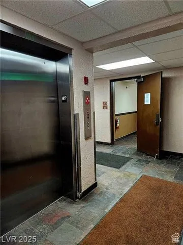 Hall with stone tile flooring, elevator, and a drop ceiling