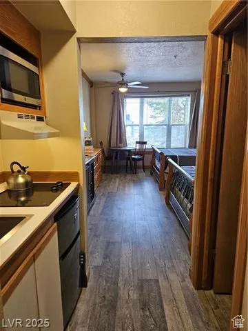 Kitchen with exhaust hood, stainless steel microwave, dark wood-type flooring, ceiling fan, and light countertops