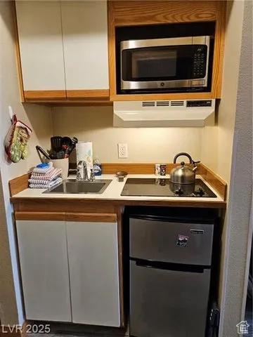 Kitchen featuring stainless steel microwave, under cabinet range hood, black electric stovetop, and white cabinetry