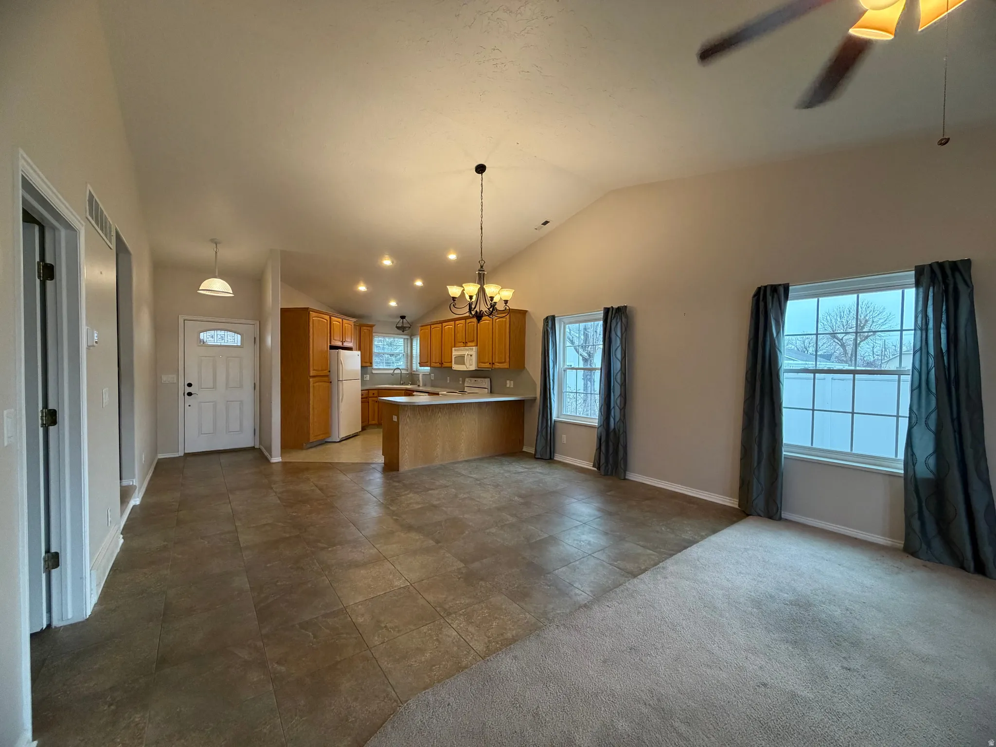 Kitchen featuring open floor plan, lofted ceiling, a chandelier, light countertops, and white appliances
