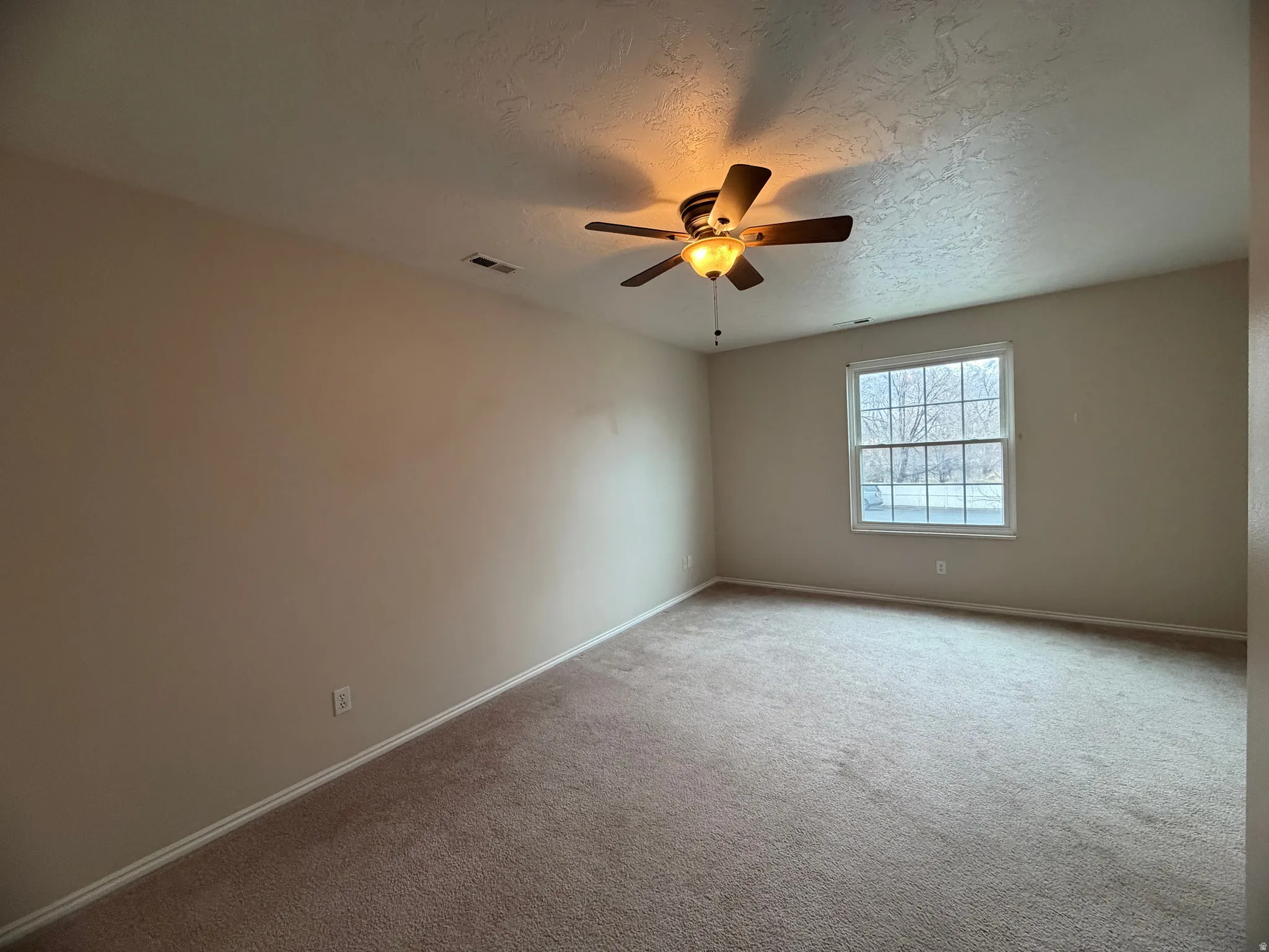 Carpeted empty room with a textured ceiling and a ceiling fan