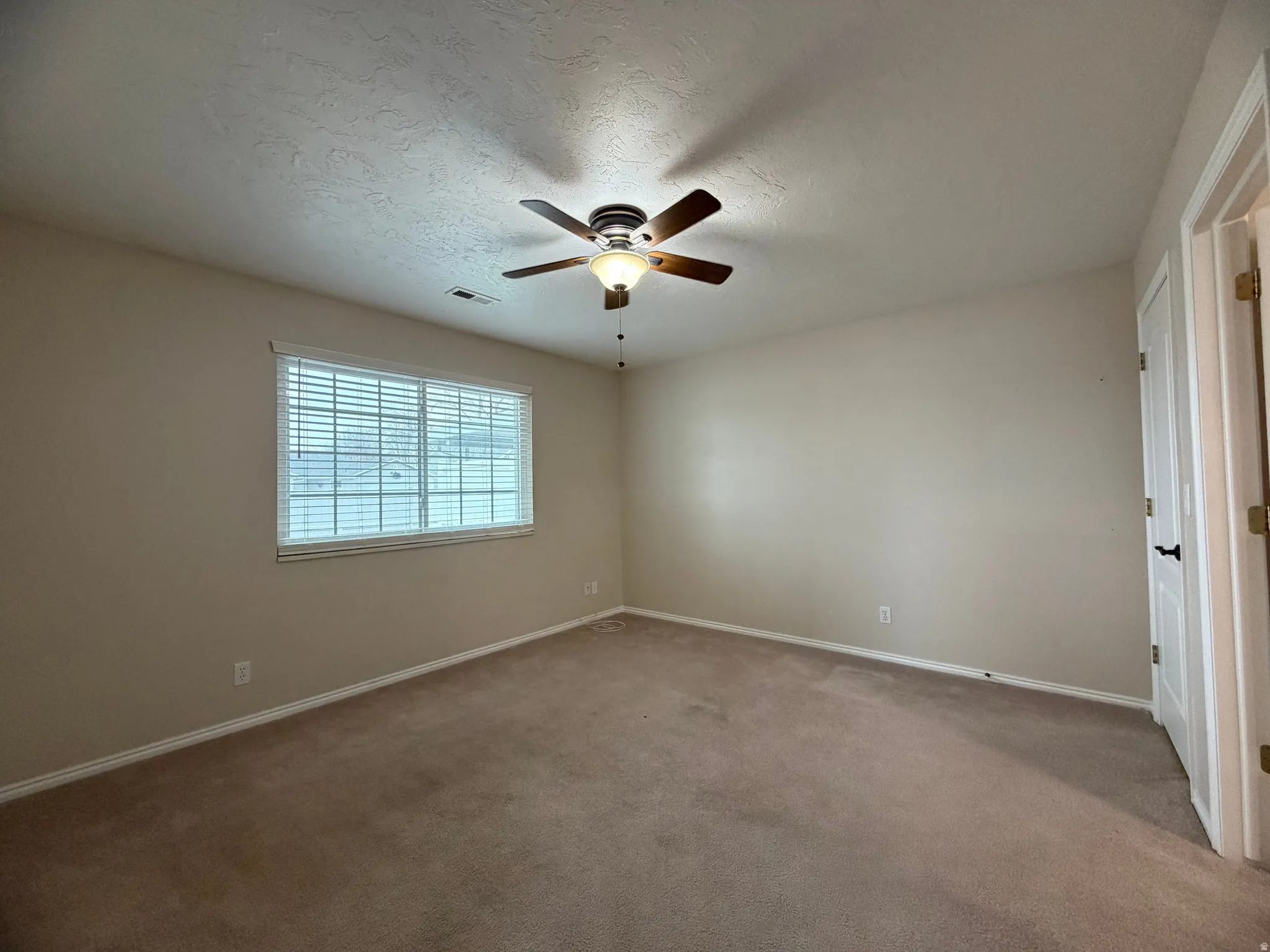 Carpeted empty room with a textured ceiling and a ceiling fan