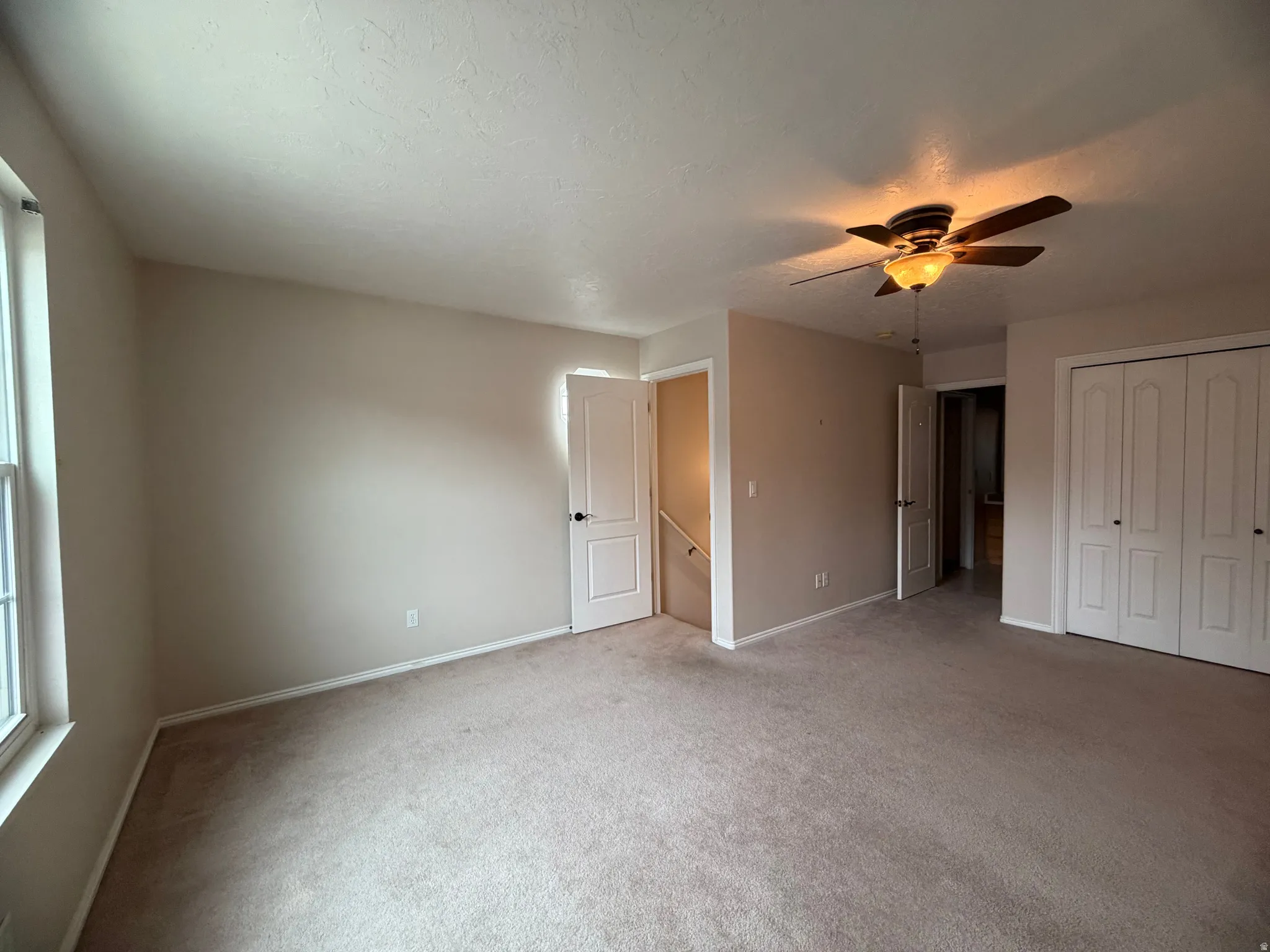 Unfurnished bedroom with light colored carpet, ceiling fan, a closet, and a textured ceiling
