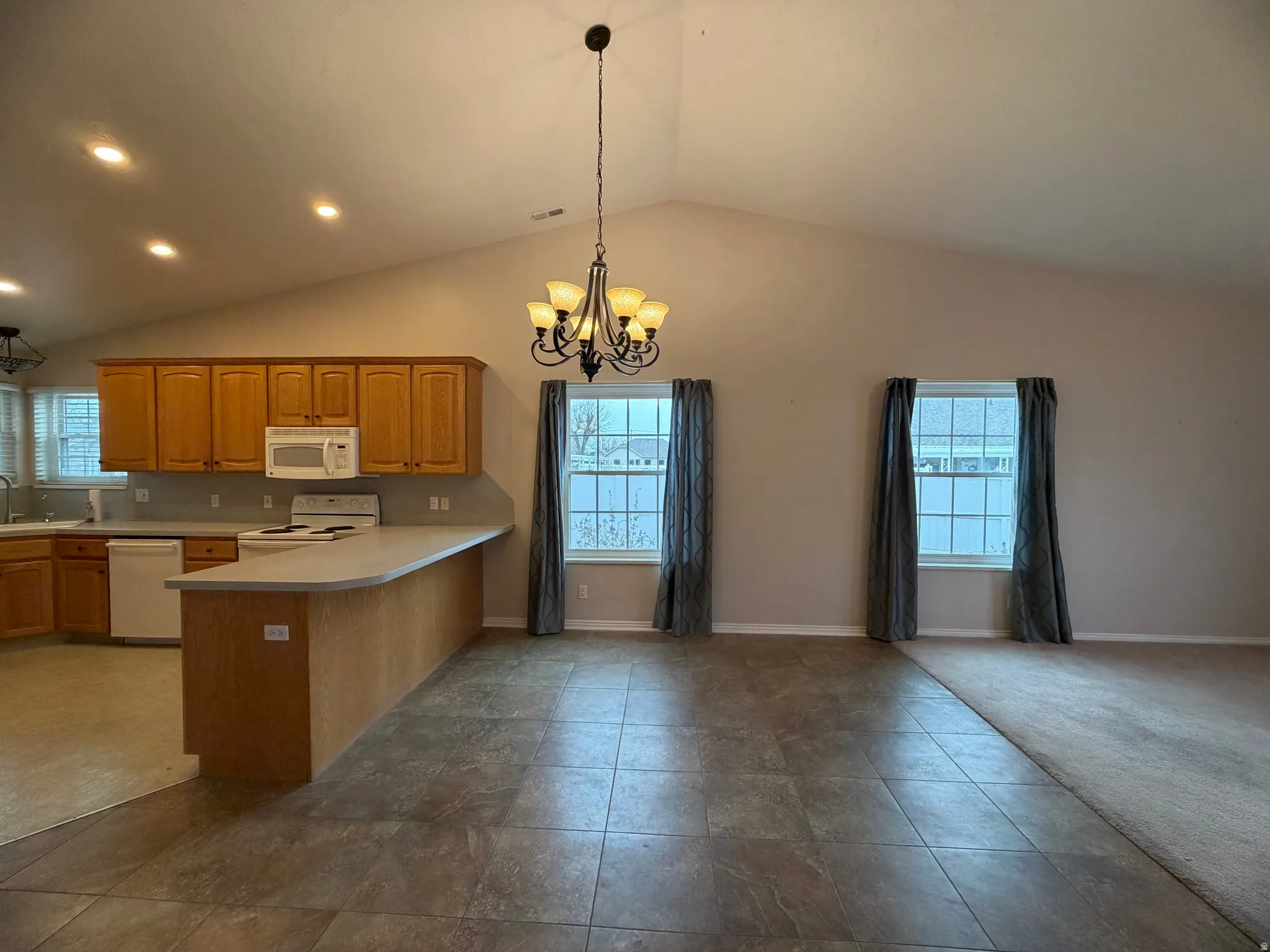 Kitchen with light countertops, hanging lights, white appliances, open floor plan, and lofted ceiling