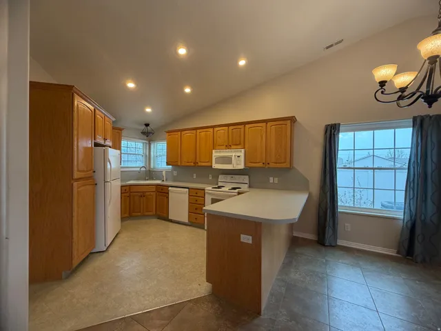 Kitchen featuring light countertops, vaulted ceiling, white appliances, a chandelier, and a peninsula