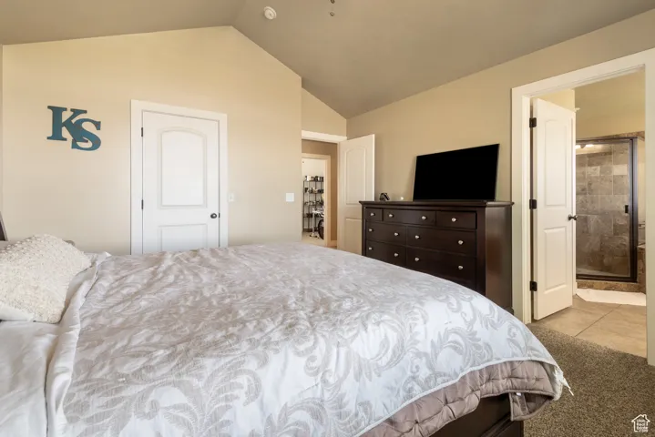 Bedroom with lofted ceiling, ensuite bathroom, tile patterned floors, and carpet
