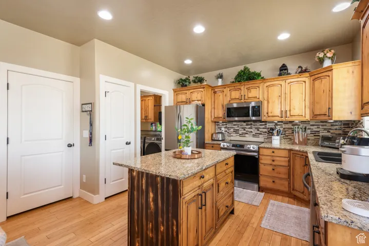 Kitchen with stainless steel appliances, washer / dryer, backsplash, light wood finished floors, and recessed lighting