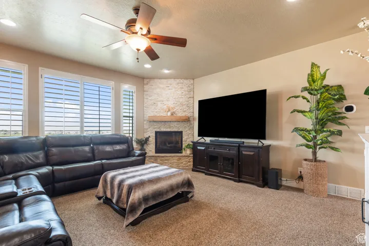 Living area with carpet, a ceiling fan, a fireplace, a textured ceiling, and recessed lighting