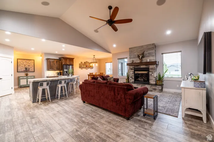 Living room with ceiling fan, light wood-style floors, a stone fireplace, recessed lighting, and high vaulted ceiling