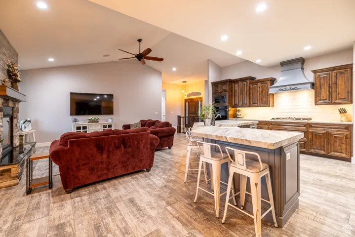 Kitchen featuring custom range hood, a kitchen bar, a stone fireplace, light countertops, and a ceiling fan