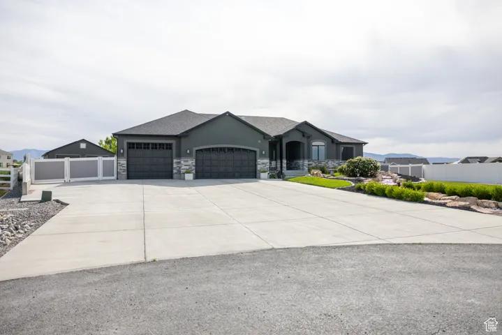 View of front facade with an attached garage, driveway, stucco siding, and stone siding