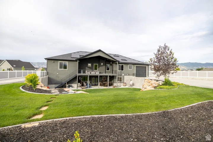 Rear view of house with stairs, roof mounted solar panels, a patio, a deck with mountain view, and an attached garage