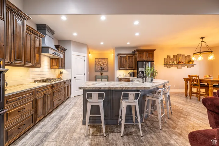 Kitchen featuring stainless steel appliances, ventilation hood, light countertops, a kitchen breakfast bar, and backsplash