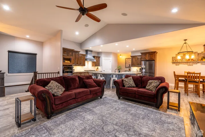 Living area with ceiling fan, a chandelier, vaulted ceiling, recessed lighting, and light wood-style flooring