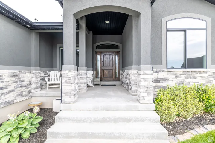 Doorway to property with stucco siding, stone siding, and a porch