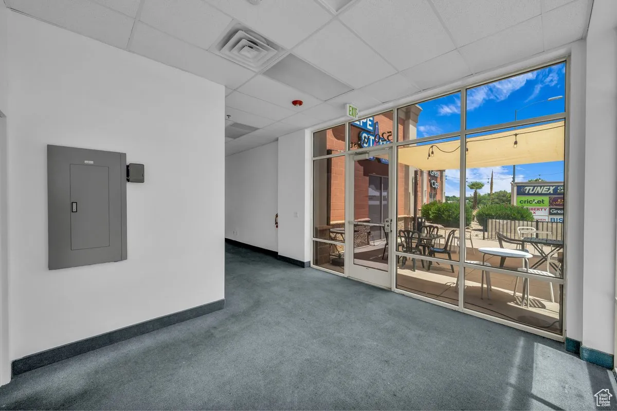 Carpeted empty room featuring electric panel, floor to ceiling windows, and a drop ceiling