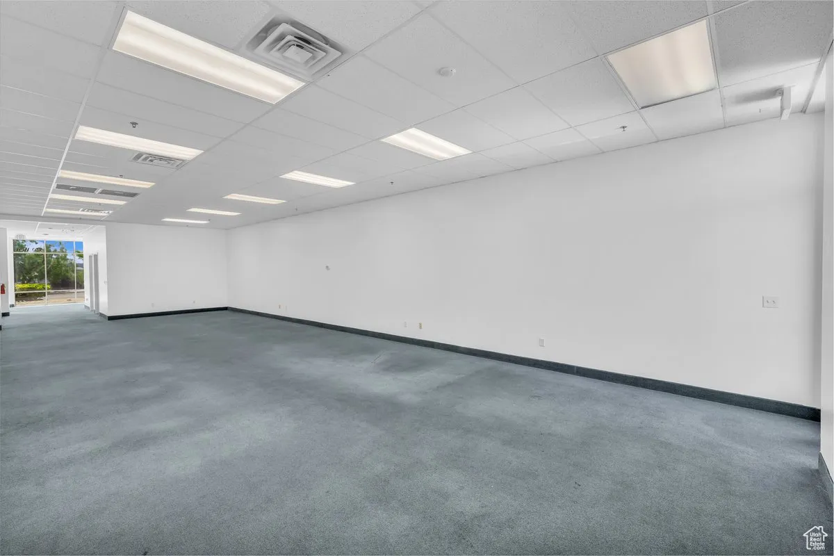 Carpeted spare room with baseboards and a drop ceiling