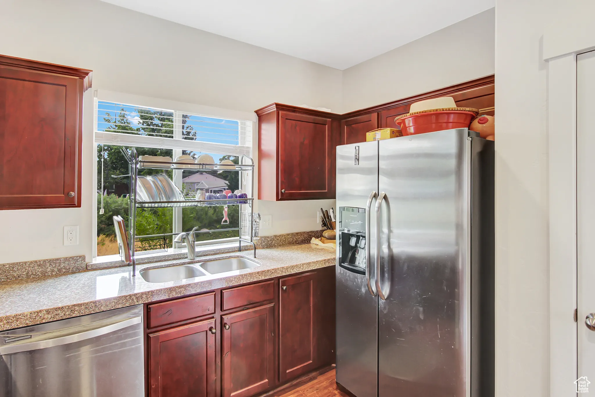 Kitchen with appliances with stainless steel finishes, dark brown cabinets, light stone counters, and wood finished floors
