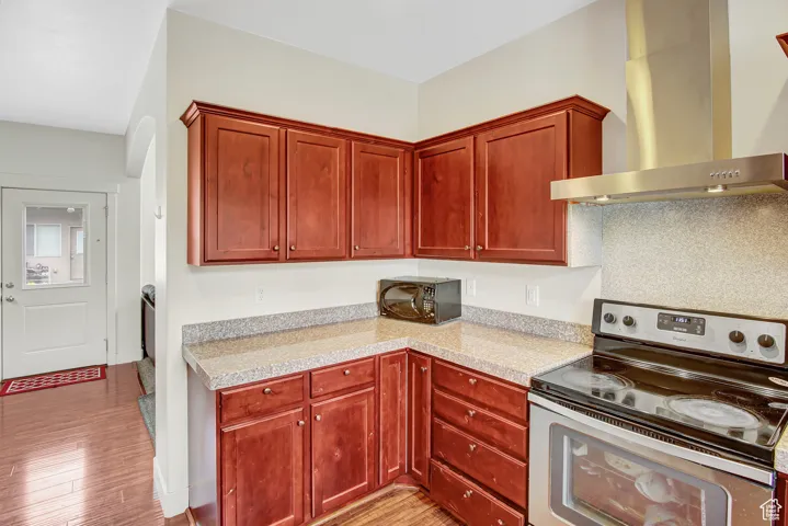 Kitchen with stainless steel electric range, wall chimney exhaust hood, black microwave, light countertops, and light wood finished floors