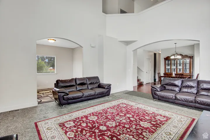 Carpeted living room featuring arched walkways, a chandelier, a towering ceiling, and stairs