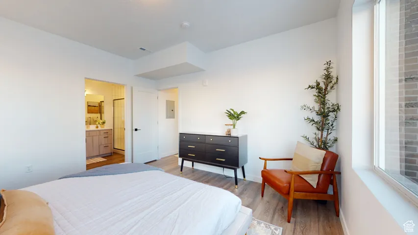 Bedroom featuring light wood-type flooring, electric panel, and ensuite bath