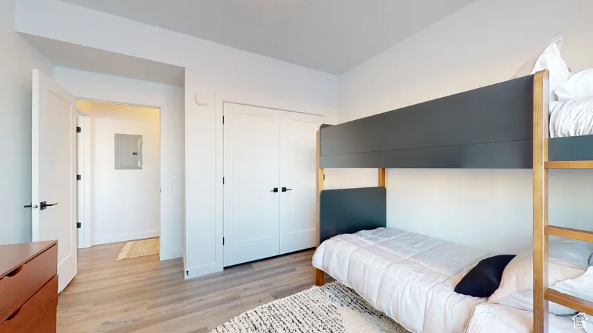 Bedroom featuring electric panel, light wood-type flooring, and a closet