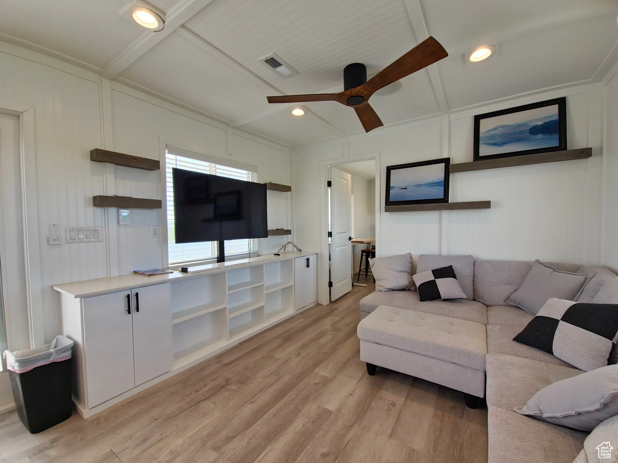 Living room with a decorative wall, light wood-style floors, ceiling fan, beamed ceiling, and recessed lighting
